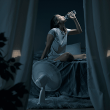 Žena sedí v noci na posteli a pije vodu